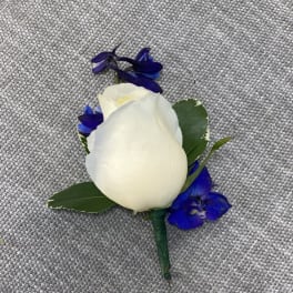 White rose boutonniere with blue accent flowers on gray fabric