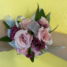 Pink rose wrist corsage with purple accent flowers and silver ribbon