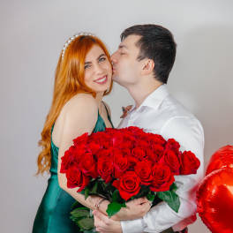 Couple holding a large bouquet of red roses with red heart balloons