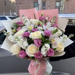 Bouquet of white roses, pink lisianthus, and white orchids wrapped in pink paper