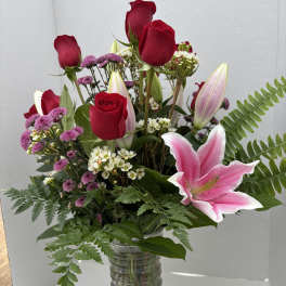 Mixed bouquet of red roses, pink lilies, and purple flowers in a glass vase