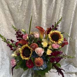 Mixed bouquet with sunflowers, roses, calla lilies, and orchids in a glass vase