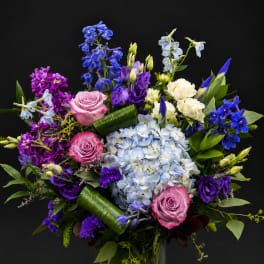 Mixed bouquet of roses, hydrangea, and purple blooms in a glass vase