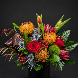 Tropical bouquet with red roses, orange pincushion blooms, and a black vase