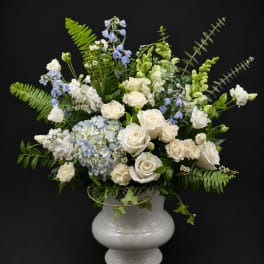 White roses and blue flowers arranged in a white urn vase