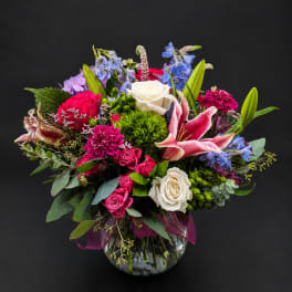 Colorful bouquet of roses, lilies, and blue flowers in a glass vase