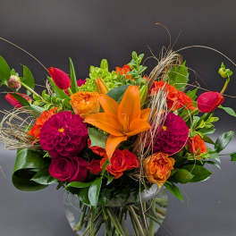 Bright mixed bouquet with orange lilies, red tulips, and magenta dahlias in a glass vase