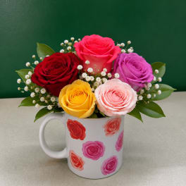 Colorful roses arranged in a white mug with small white filler flowers