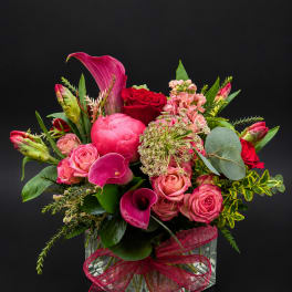 Pink and red floral arrangement in a clear glass vase with a ribbon