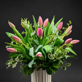 Pink tulips arranged in a tall white vase with mixed greenery