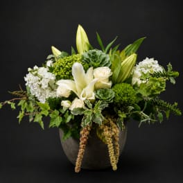 White lilies and roses arranged in a dark vase with green succulents