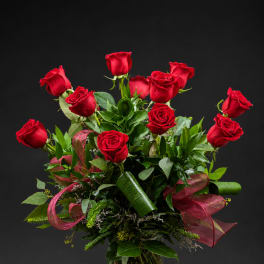 Red roses arranged in a clear glass vase with ribbon accents