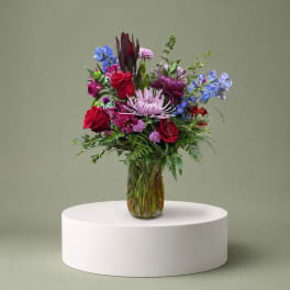 Mixed bouquet of red, purple, and blue flowers in a glass vase