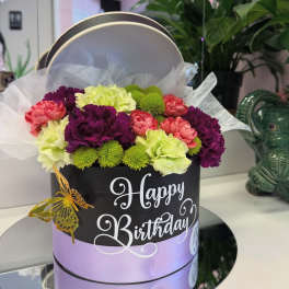 Birthday flower arrangement in a round gift box with pink, purple, and green blooms