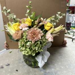Mixed bouquet in a glass vase with yellow roses, lilies, and pale pink blooms