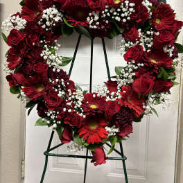 Heart-shaped wreath of red roses and gerbera daisies on a stand