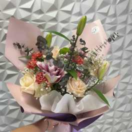 Handheld bouquet of roses, lilies, and carnations wrapped in pink and purple paper
