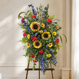 Tall mixed flower arrangement with sunflowers, red carnations, and blue blooms on an easel