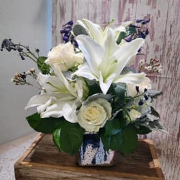 White lilies and roses arranged in a small ceramic vase