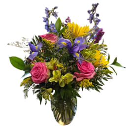 Mixed bouquet of pink roses, purple irises, and yellow flowers in a glass vase
