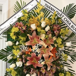 Large standing floral wreath with lilies, roses, and yellow blooms
