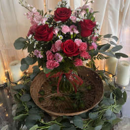 Red and pink rose arrangement in a glass vase with candles and draped fabric