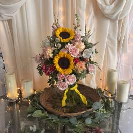 Sunflowers and pink roses arranged in a glass vase with candles nearby