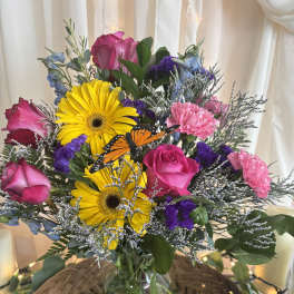 Bouquet of pink roses, yellow gerbera daisies, and purple flowers in a glass vase