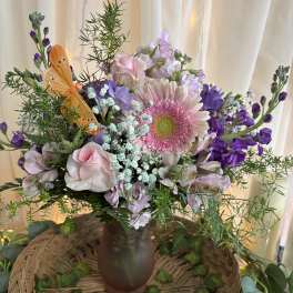Pink and purple mixed bouquet in a brown vase with an orange butterfly