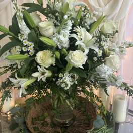 White lilies and roses arranged in a glass vase with greenery