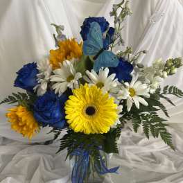 Bouquet of blue roses, white daisies, and yellow gerbera daisies in a glass vase