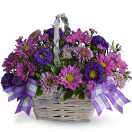Purple and pink daisy bouquet in a white wicker basket with ribbon bows
