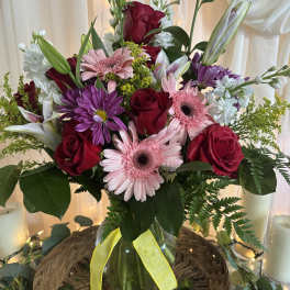 Mixed bouquet of roses, gerbera daisies, lilies, and purple daisies in a glass vase