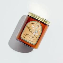 Amber glass candle jar with a gold lid and illustrated label