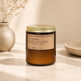 Amber jar candle with a gold lid and label reading teakwood and tobacco