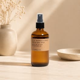 Amber room spray bottle on a neutral tabletop with a vase and bowl nearby