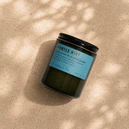 Black jar candle with a blue label on a beige surface