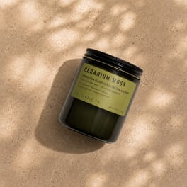 Black jar candle with a green label on a beige surface