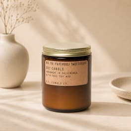 Amber jar candle with a gold lid and label on a neutral tabletop
