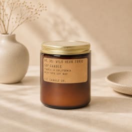 Amber jar candle with a gold lid on a beige surface