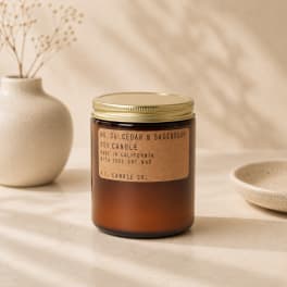 Amber jar candle with a gold lid beside a ceramic vase