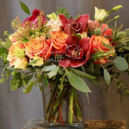 Mixed bouquet of orange and red flowers in a clear glass vase