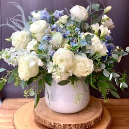 White and pale blue floral arrangement in a white vase