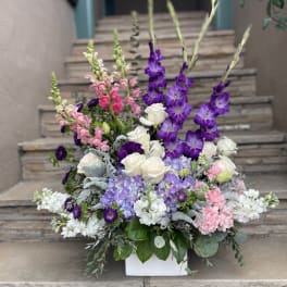 Tall floral arrangement with purple, pink, and white blooms in a white container
