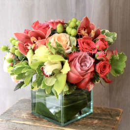 Mixed pink and red flower arrangement in a square glass vase