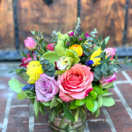 Colorful mixed bouquet of roses, tulips, orchids, and ranunculus in a clear glass vase