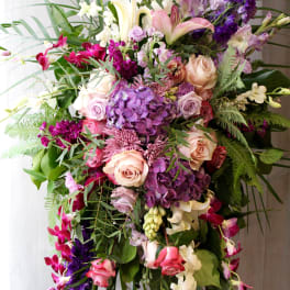 Large mixed floral arrangement with roses, lilies, orchids, and purple hydrangea