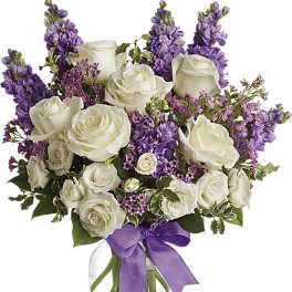 White roses and purple flowers in a glass vase with a purple ribbon