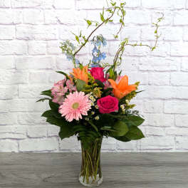 Mixed bouquet in a clear glass vase with pink, orange, and blue flowers