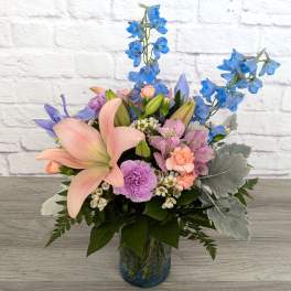 Pastel bouquet with pink lilies and blue delphinium in a glass vase